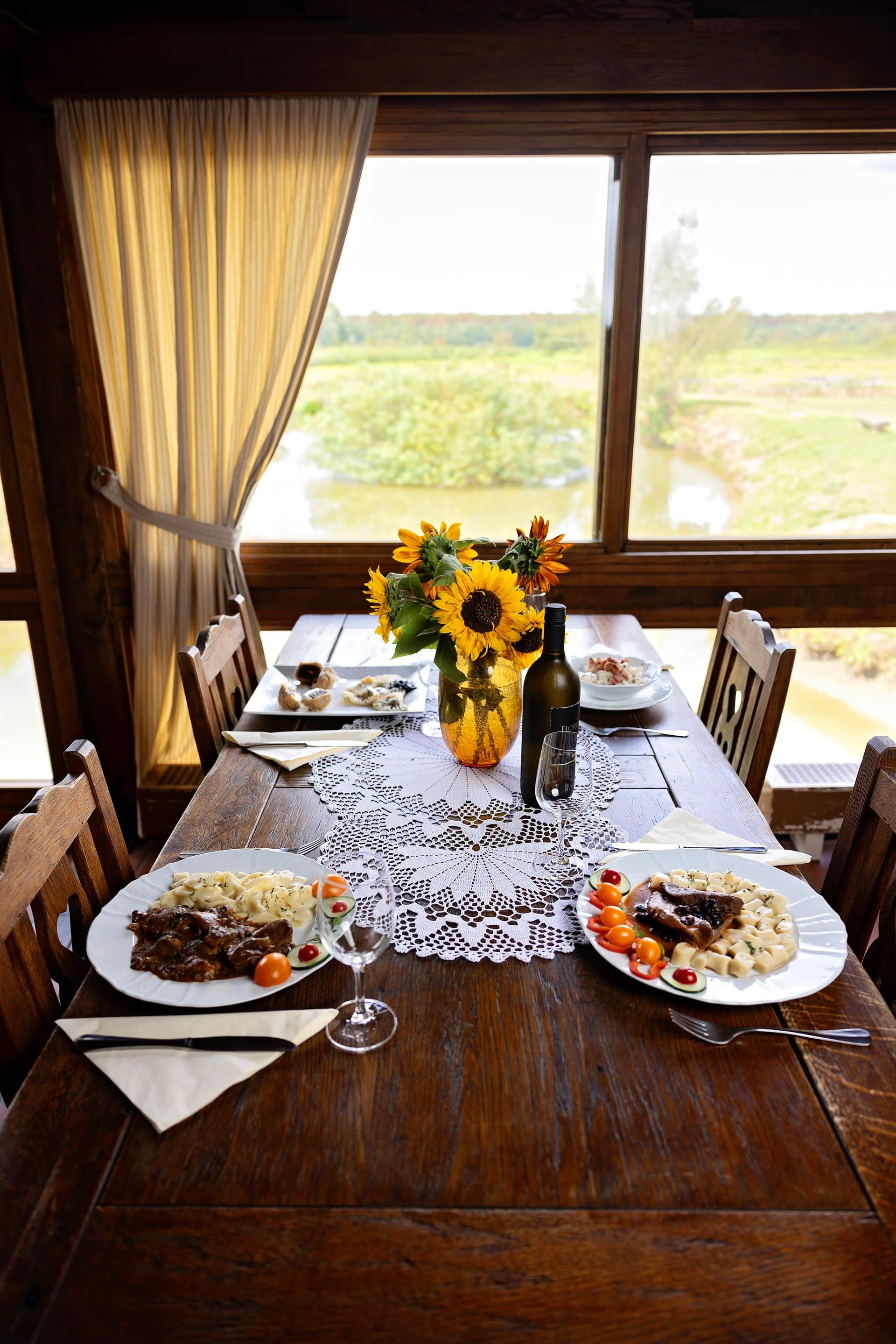 Postavljen stol s jelima i sunčanicama, uz pogled na vodu i zelenilo kroz prozor